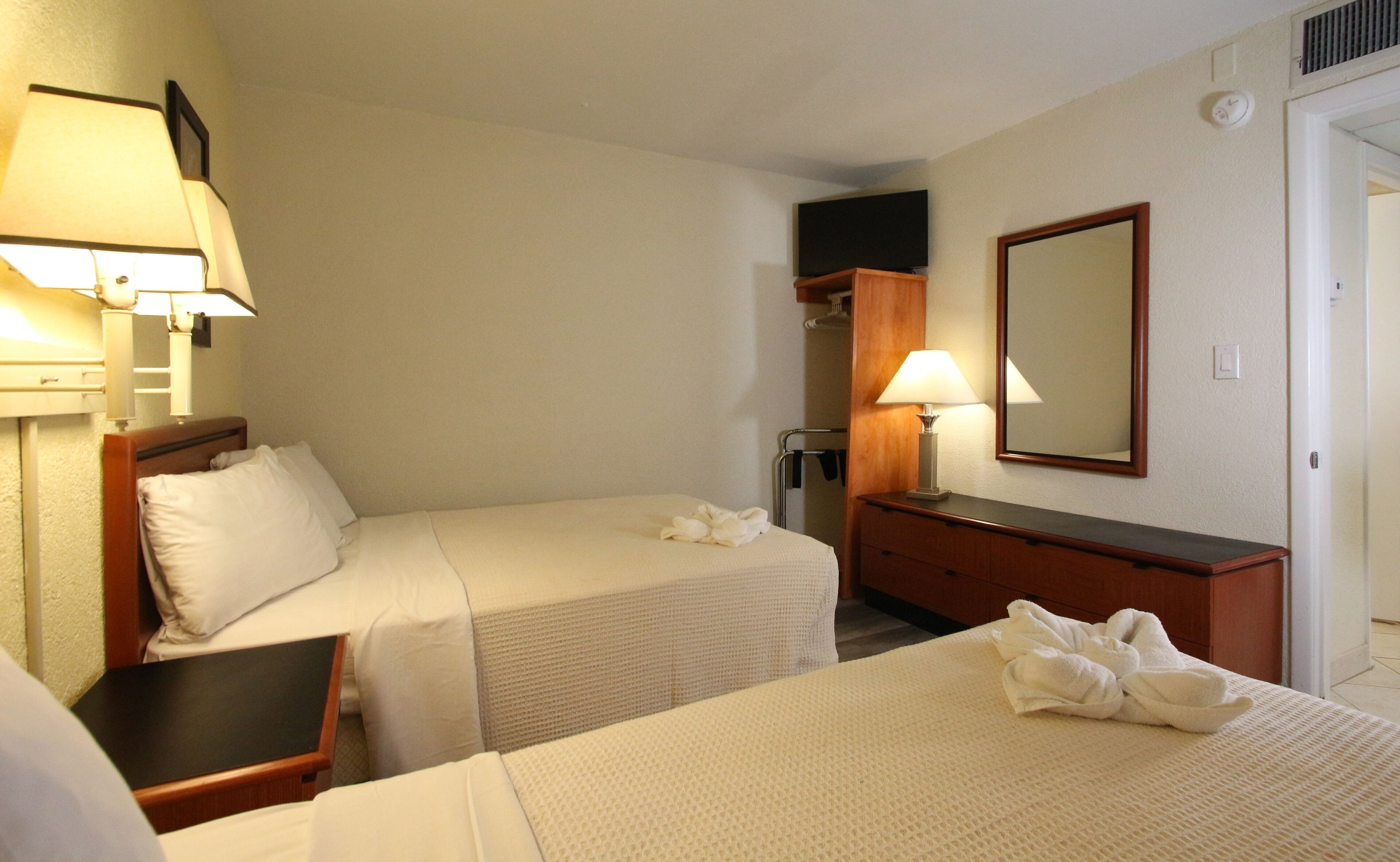Una habitación de hotel con dos camas, un aparador, un espejo y una lámpara.