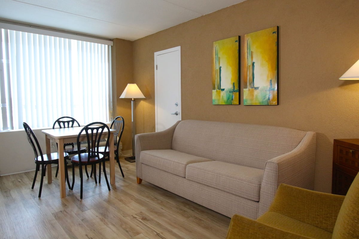Ein Wohnzimmer mit einem beigen Sofa, einem Esstisch mit Stühlen und zwei Bildern an der Wand.