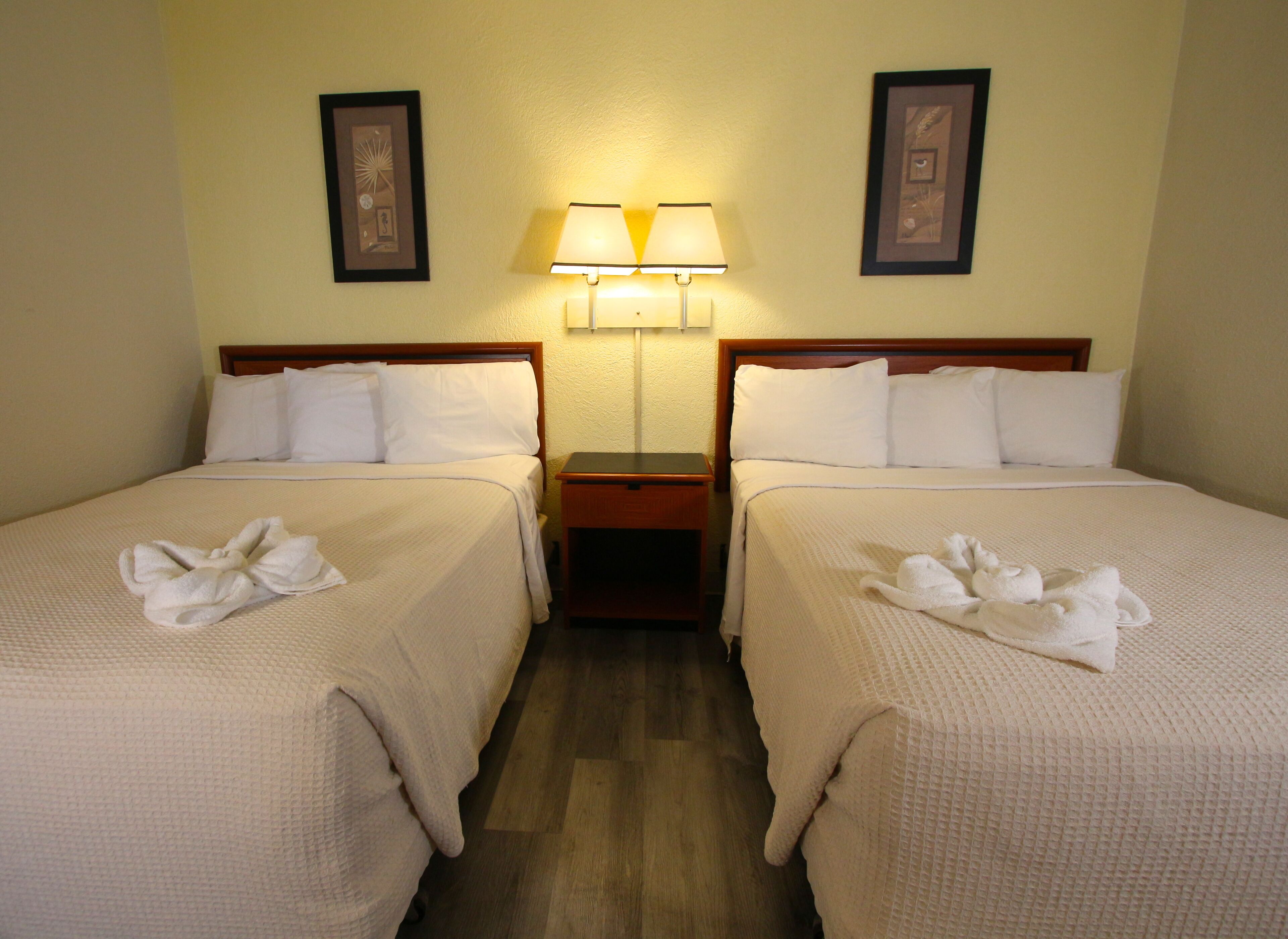 Une chambre d’hôtel avec deux lits, chacun équipé de draps et de serviettes blancs. Une table de chevet avec une lampe se trouve entre les deux lits.