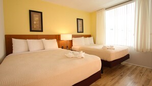 Een hotelkamer met twee bedden, houten hoofdeinden en een groot raam met gordijnen.