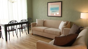 Een woonkamer met een beige bank, twee fauteuils, een eettafel met stoelen en een ingelijste foto aan de muur.