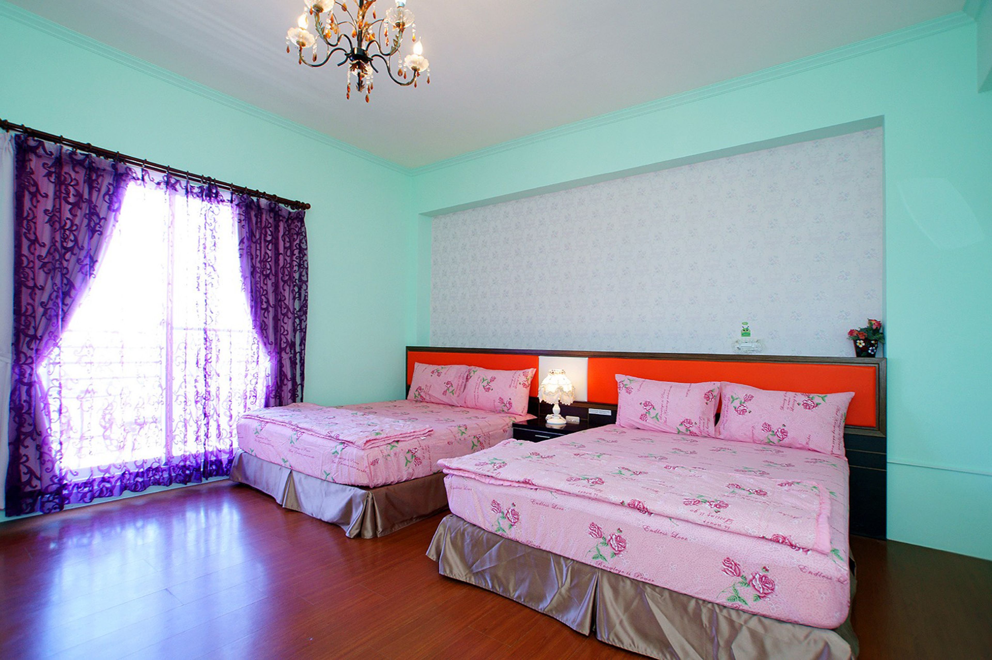 A bedroom with two beds, a chandelier, and a window with purple curtains.
