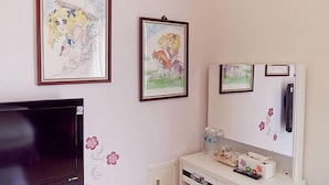 A room with a TV, framed artwork on the wall, a small cabinet with items, and a refrigerator. - The Garden Rose B&B (Taitung)