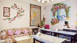 A cozy living room with a sofa, a dining table, and a decorative wall mural. - The Garden Rose B&B (Taitung)
