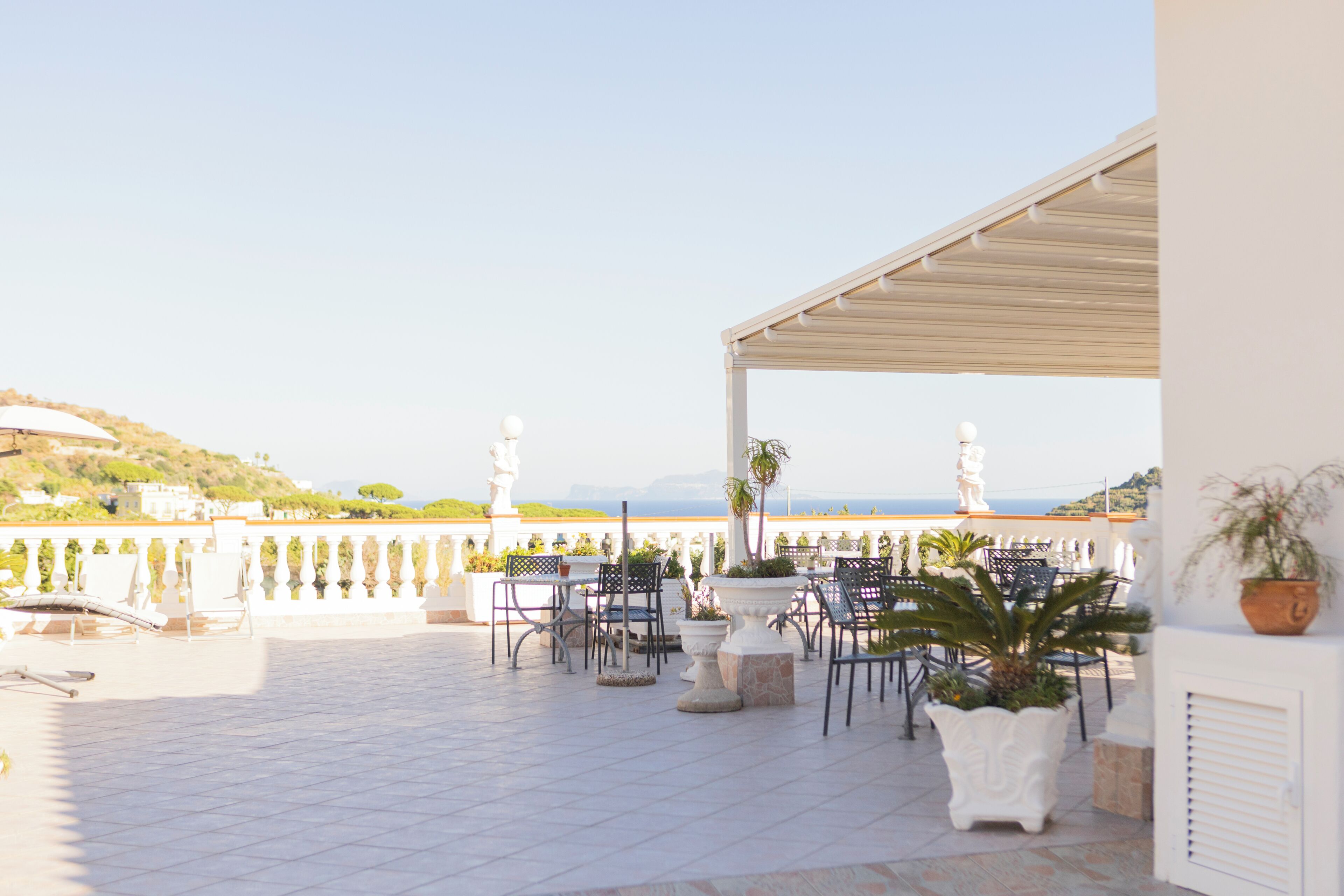 An outdoor terrace with chairs and tables, a white railing, and a view of the sea.