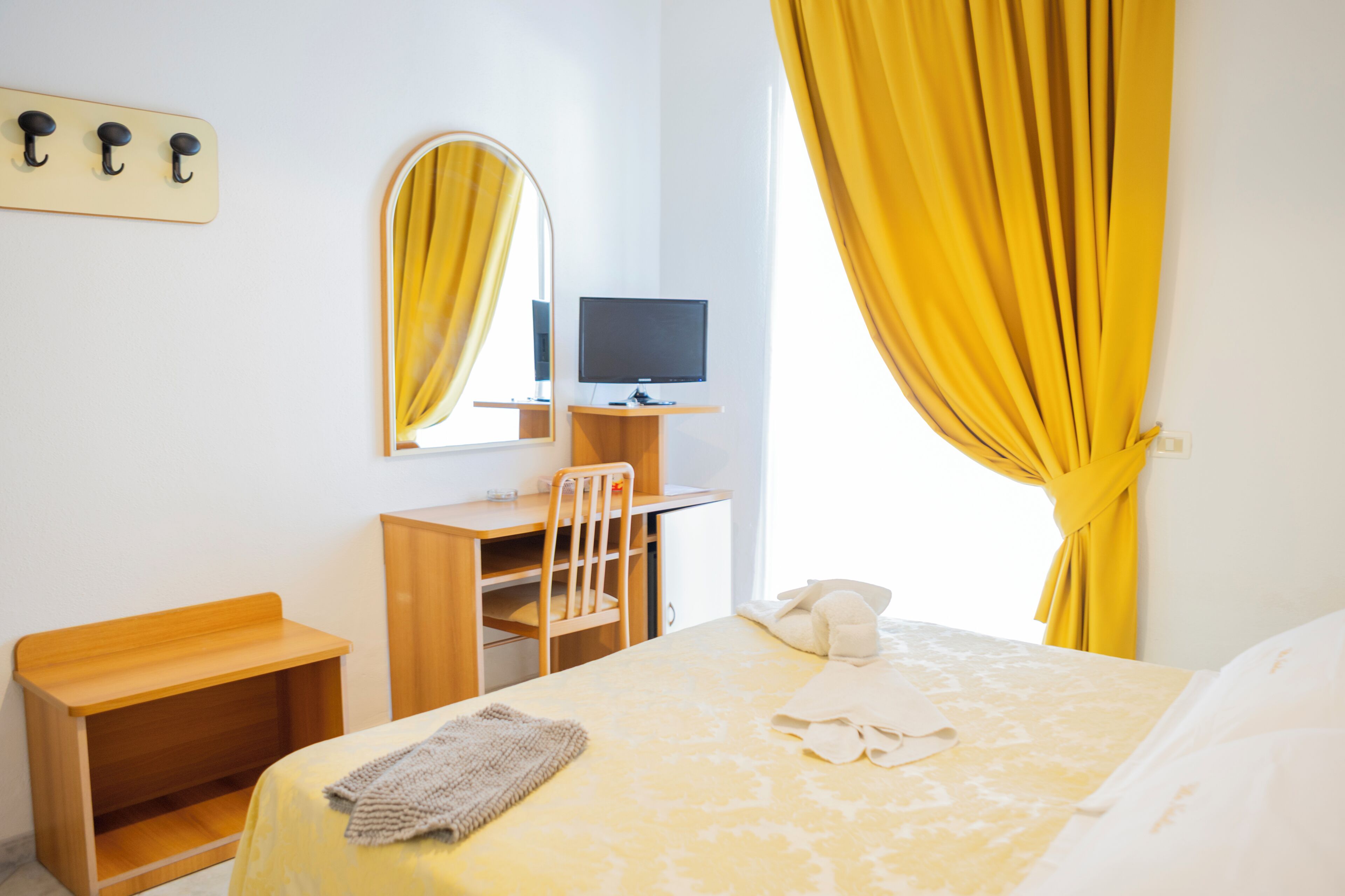 A hotel room with a bed, a desk with a computer, a chair, a mirror, and a telephone.