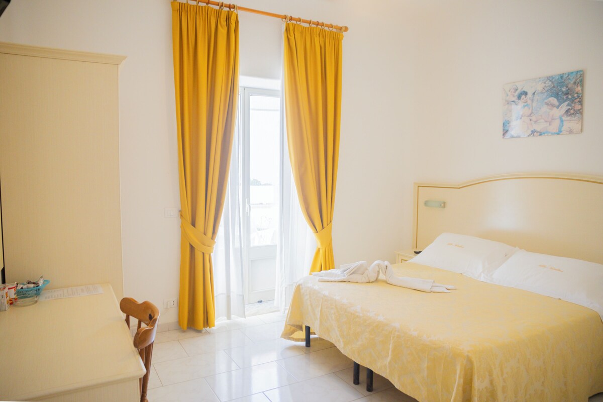 Une chambre d’hôtel avec un lit, une chaise, un bureau et une fenêtre avec des rideaux.