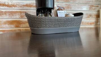 A basket containing a coffee maker, a bag of coffee, and a thank you card on a wooden table against a rustic wall.