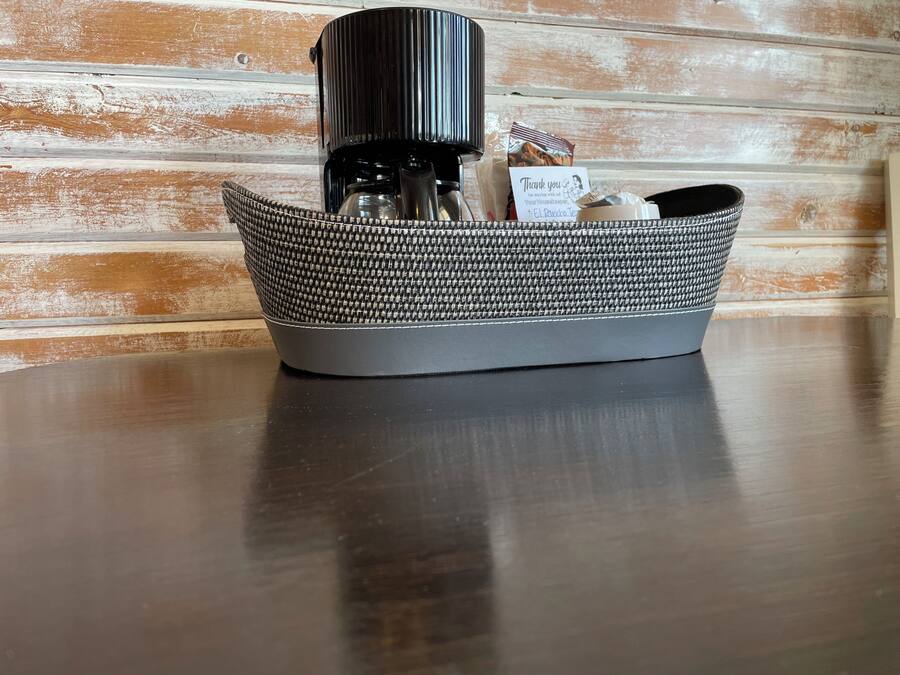 A basket containing a coffee maker, a bag of coffee, and a thank you card on a wooden table against a rustic wall.