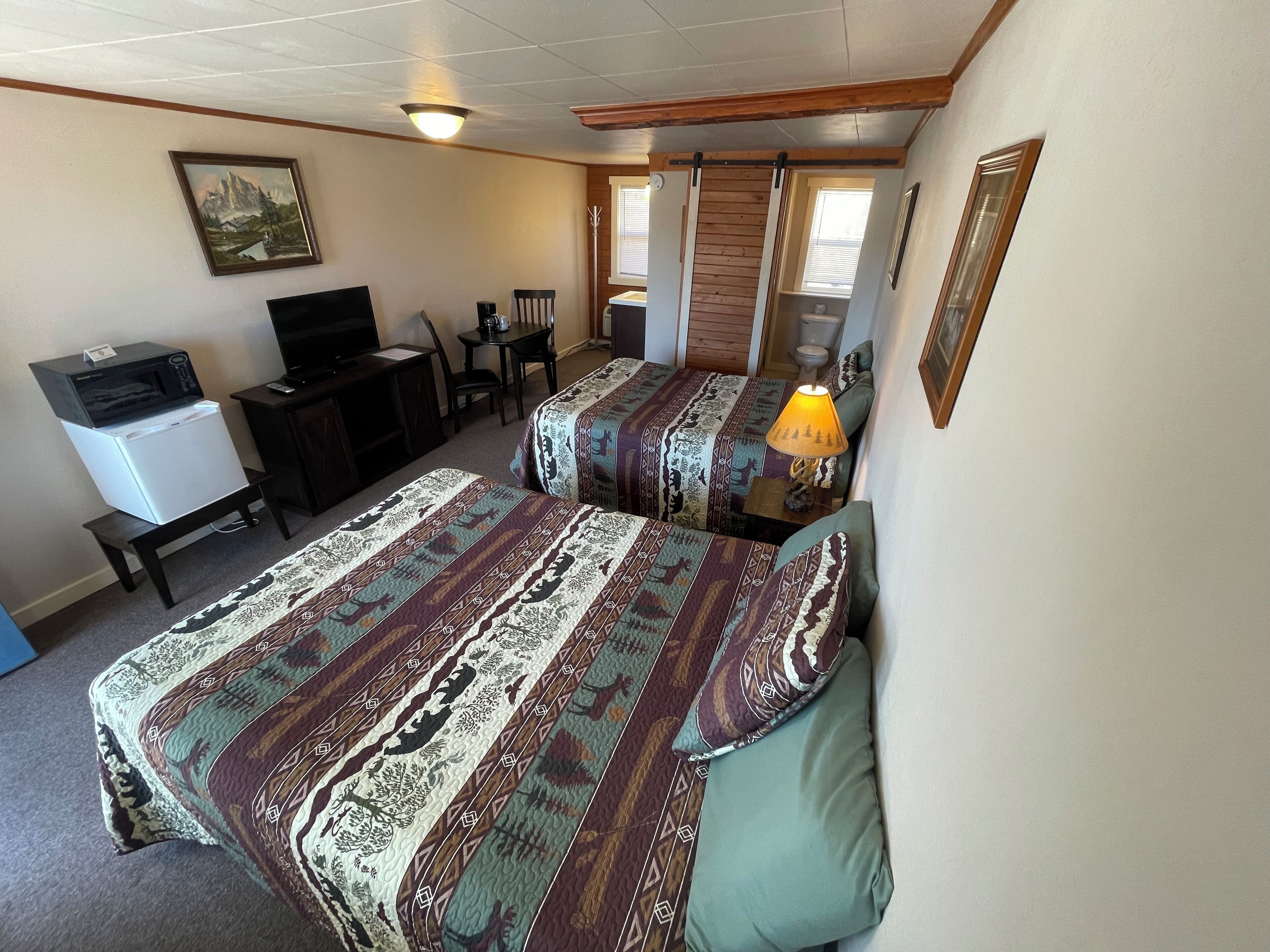 A compact hotel room with two beds, a desk, a chair, a television, and a microwave.