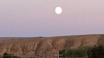 A moon in the sky above a landscape with a flat-topped hill and sparse vegetation.