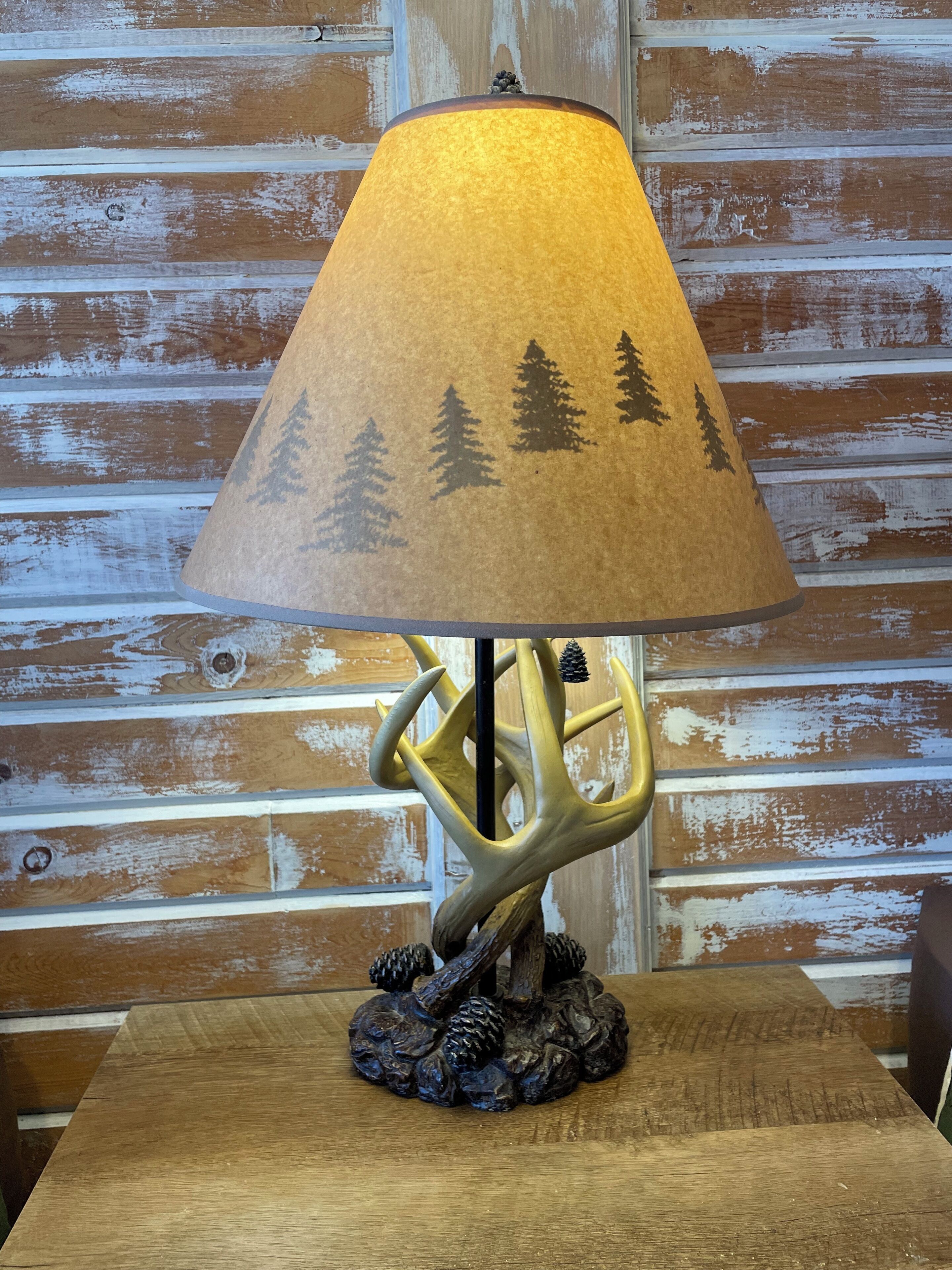 A table lamp with a forest-themed shade and a deer antler base.