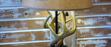 A table lamp with a forest-themed shade and a deer antler base.