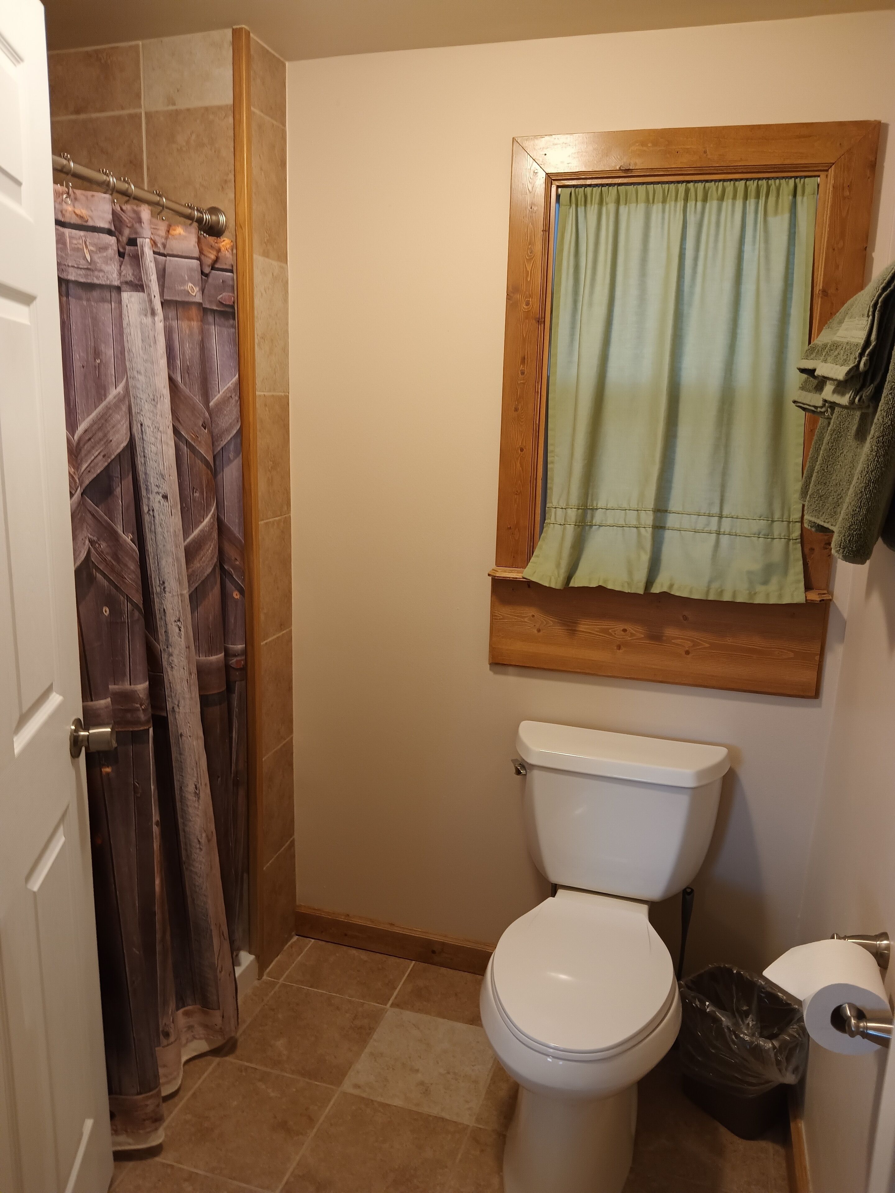 Et badeværelse med toilet, bruseforhæng, et vindue med gardin og en bøjle til håndklæder.