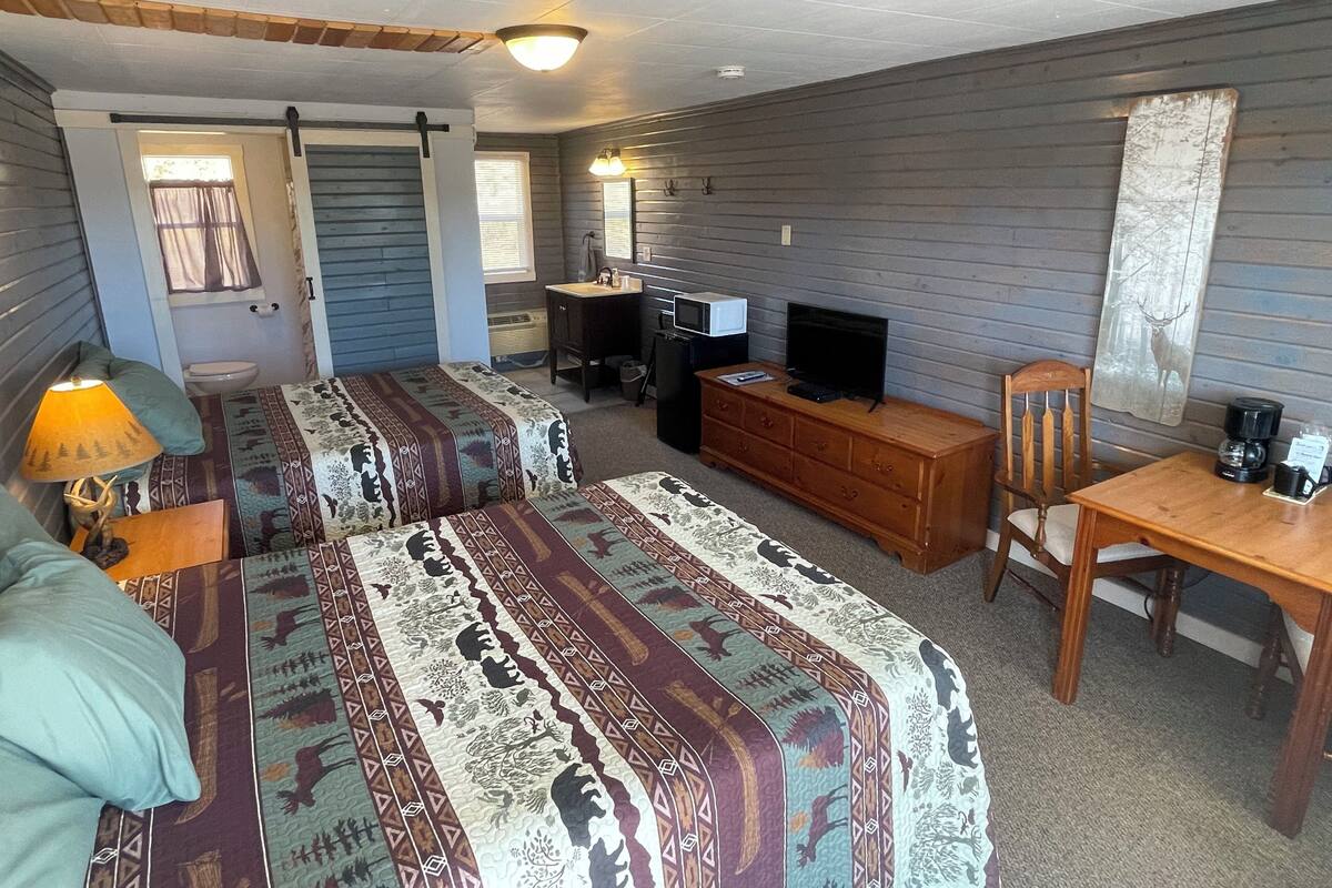 A room with two beds, a desk, a television, and a dresser.