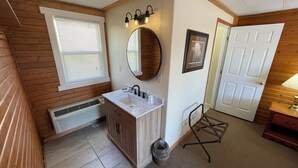 A bathroom with a wooden vanity, a sink, a mirror, a light fixture, and a door. - El Rancho Motel (Thermopolis)