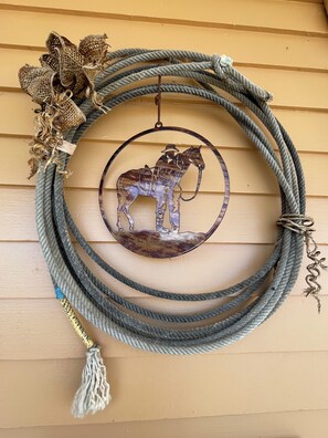 A metal horse sculpture hanging from a rope coiled on a wooden wall.