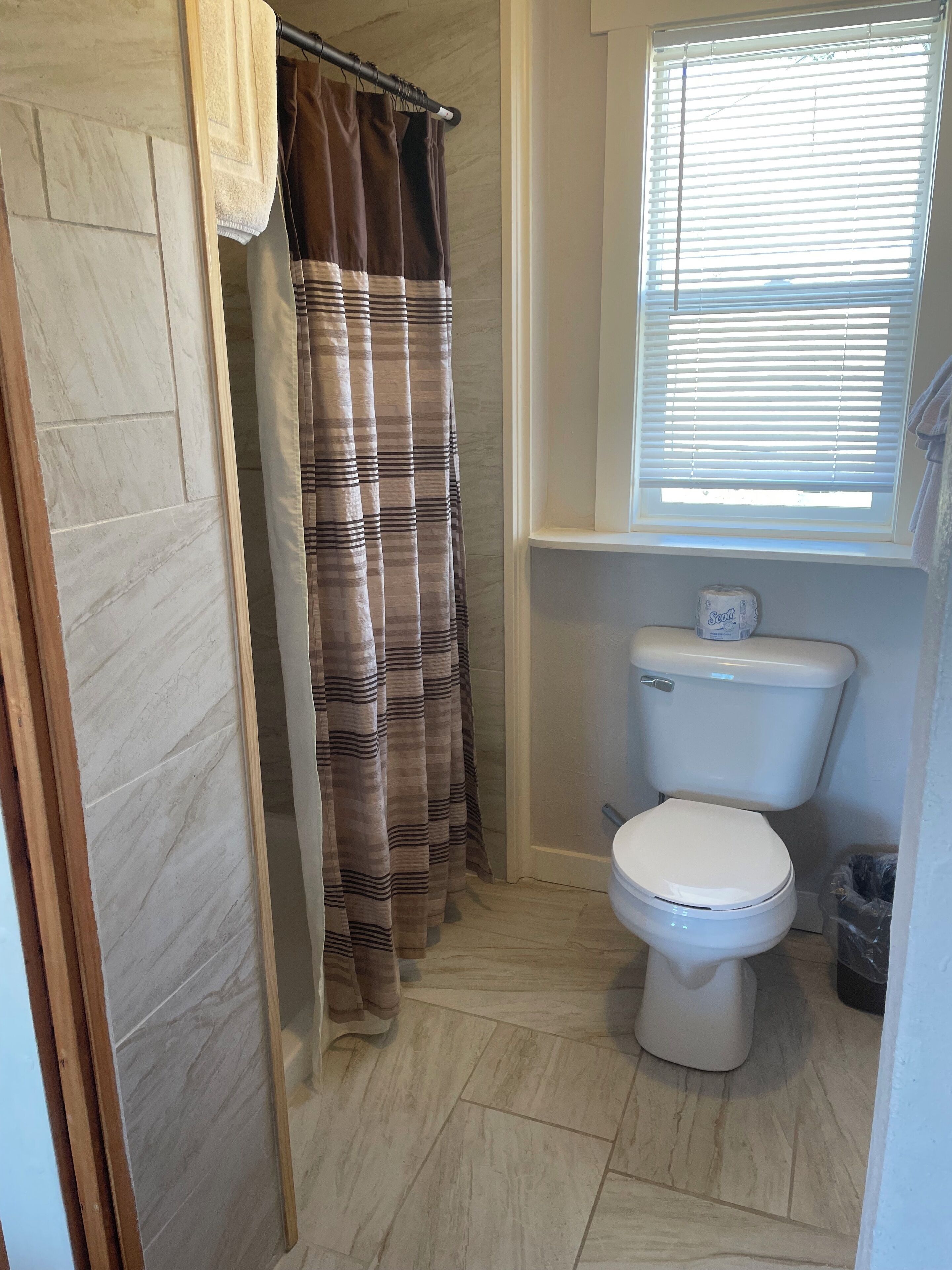 A bathroom with a toilet, a shower curtain, and a window with blinds.