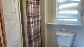 A bathroom with a toilet, a shower curtain, and a window with blinds.