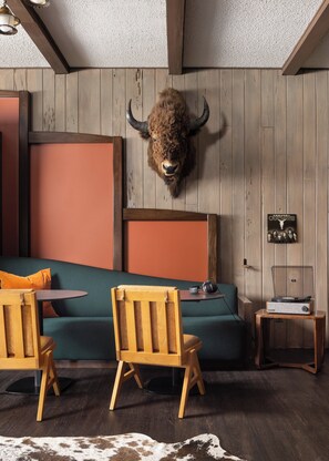 A room with a wooden wall, a mounted buffalo head, a green sofa, wooden chairs, a small table, and a record player.