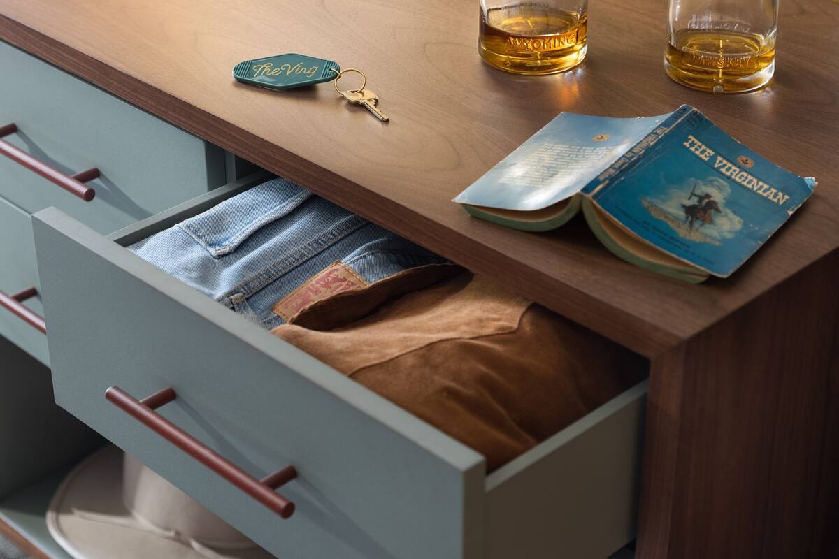A wooden table with a book titled "The Virginian," a glass of whiskey, a keychain, and a pair of keys.