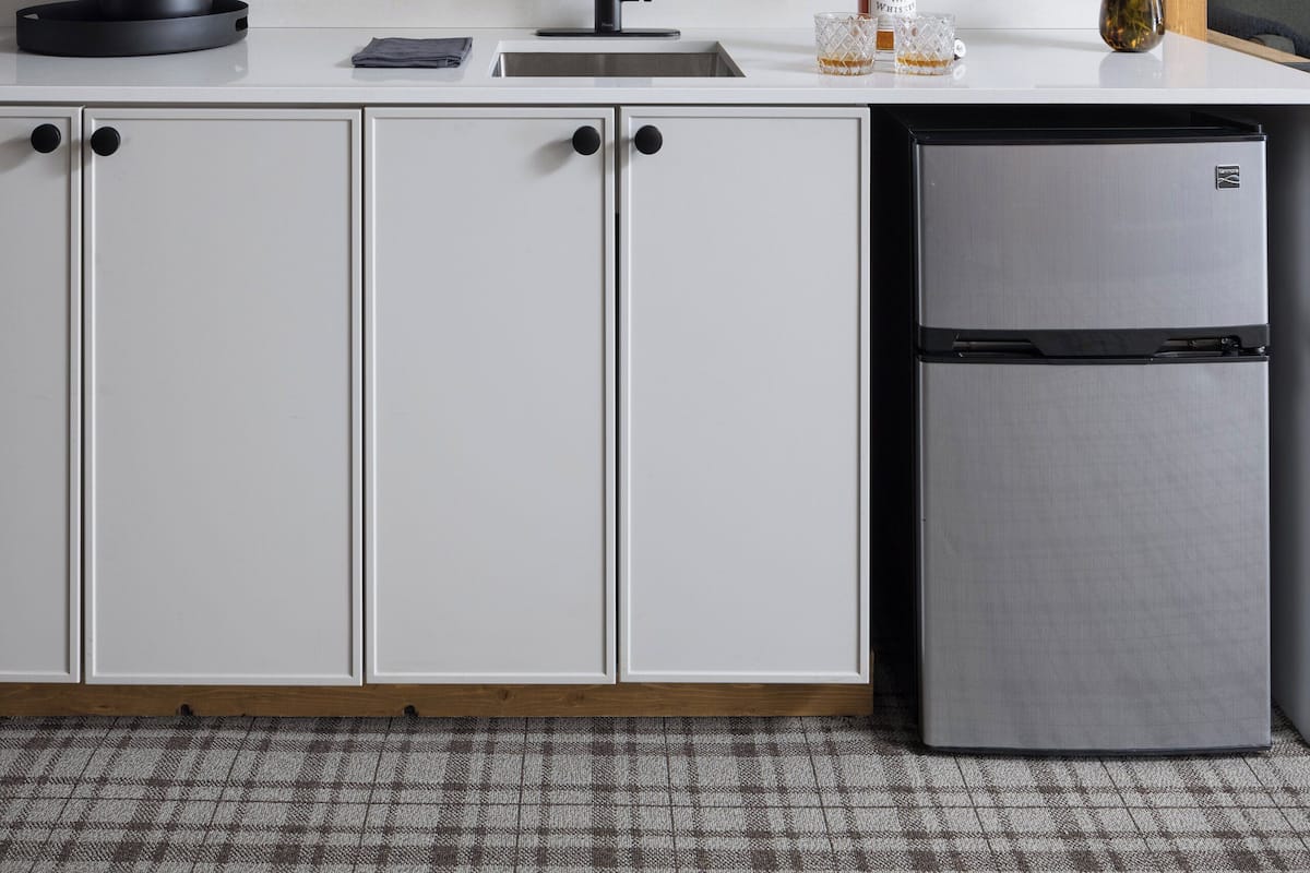 A modern kitchen with white cabinets, a stainless steel refrigerator, a microwave, and a sink.