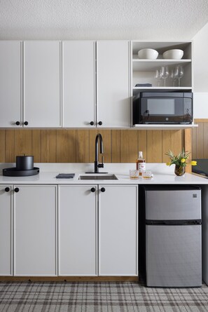 A modern kitchen with white cabinets, a stainless steel refrigerator, a microwave, and a sink.