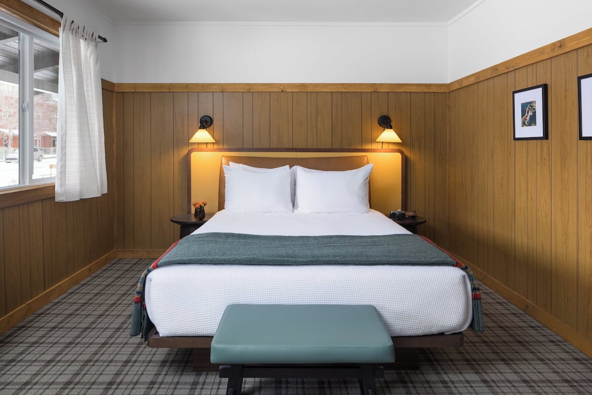A neatly arranged bedroom with a large bed, bedside tables, a bench, and a window with curtains.