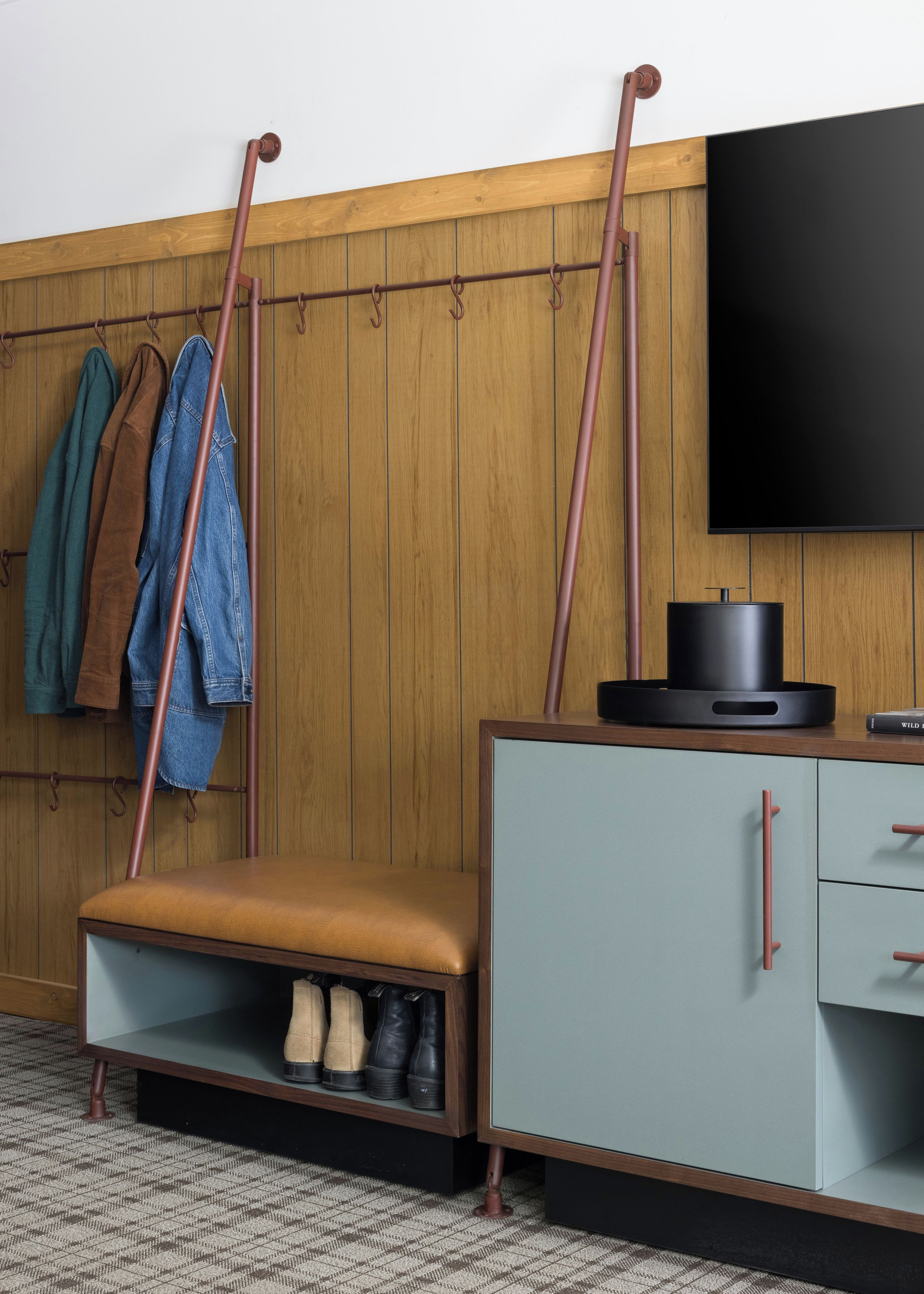 A room with a wooden wall, a mounted television, a bench with storage underneath, and a shoe rack.