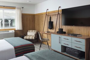 Una habitación de hotel con dos camas, un escritorio con silla, un televisor y un armario.