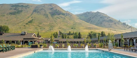 A swimming pool with a mountain backdrop, outdoor seating, and a lifeguard sign.