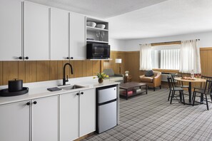 A compact kitchen with white cabinets, a microwave, and a sink. There is a dining area with a table and chairs, and a sofa.