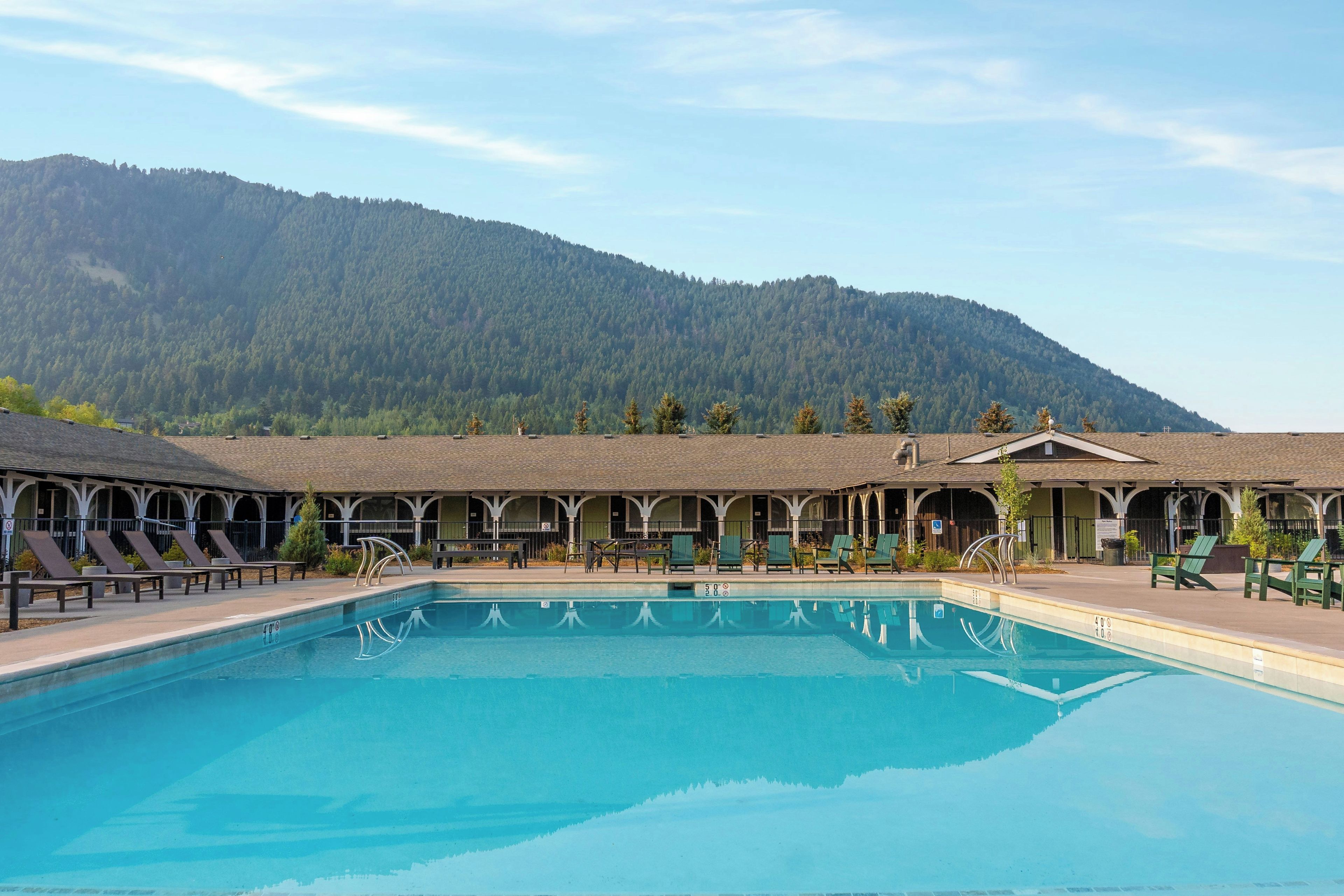 A swimming pool with lounge chairs, a covered patio area, and a mountain backdrop.