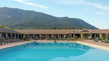 Piscina con sillas de descanso, un patio cubierto y montañas al fondo.