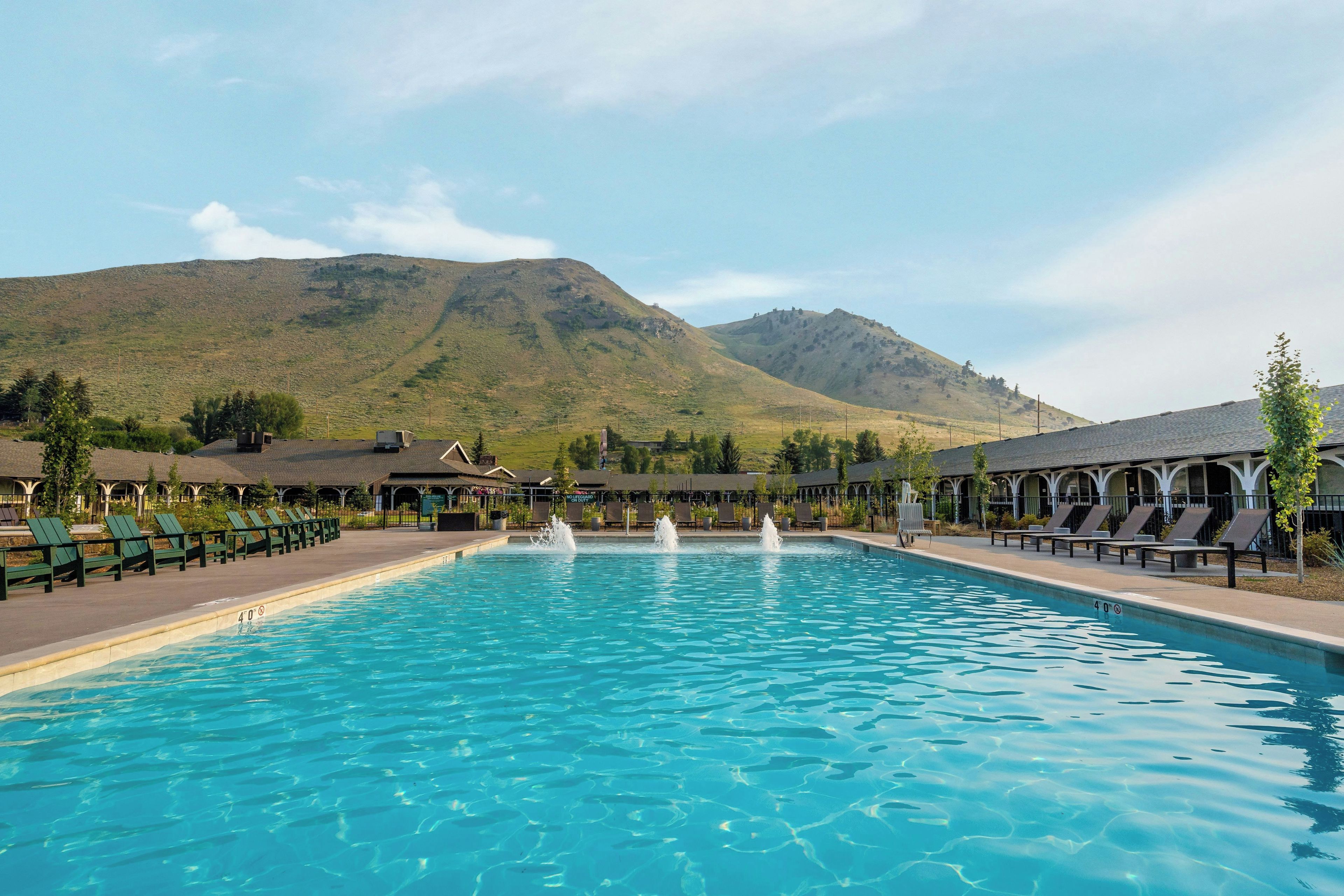 A swimming pool with a mountain backdrop, lounge chairs, and a covered seating area.