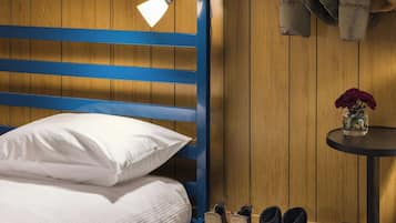A bunk bed with two lamps, a coat rack with jackets, a camera, and a small table with a vase.