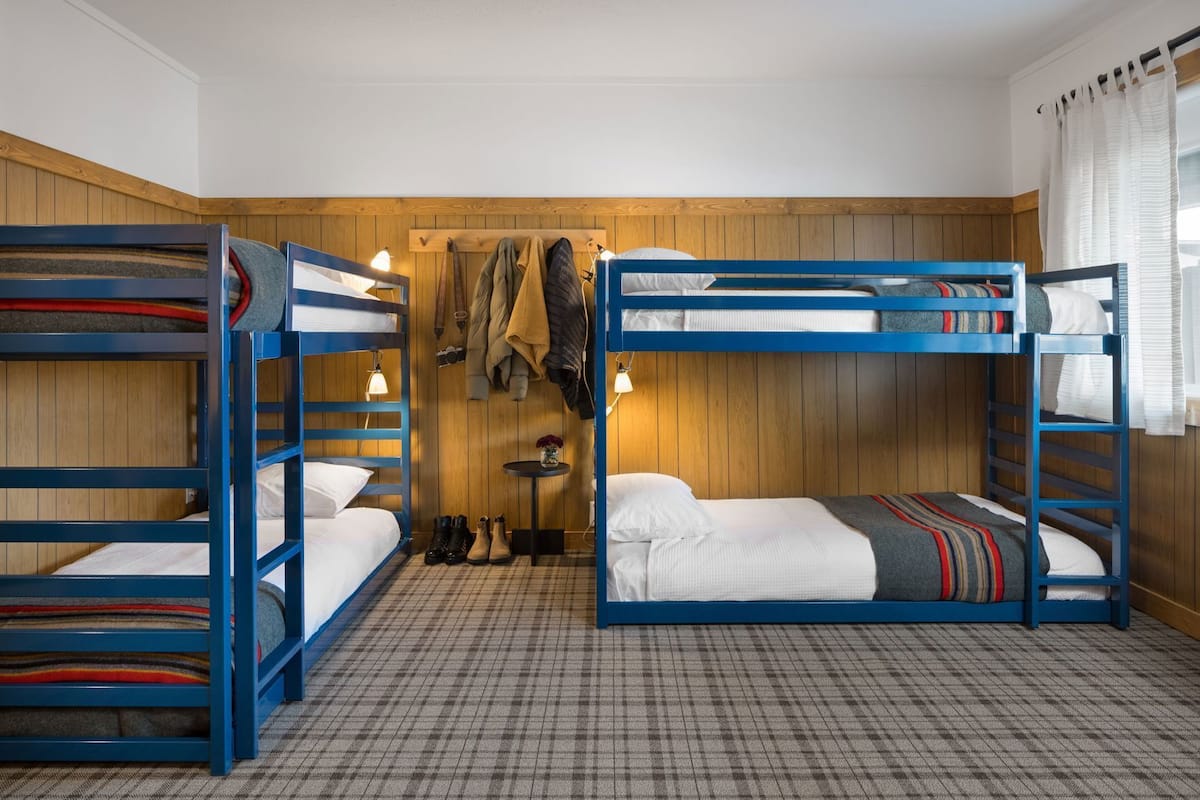 A room with bunk beds, a small table with shoes, and a coat rack.