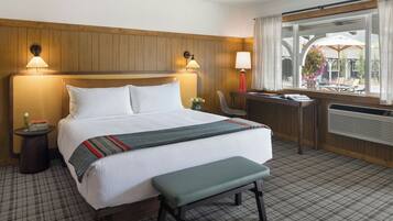 Ein Hotelzimmer mit Bett, Nachttischen, Schreibtisch, Bank und einem Fenster mit Blick ins Freie.