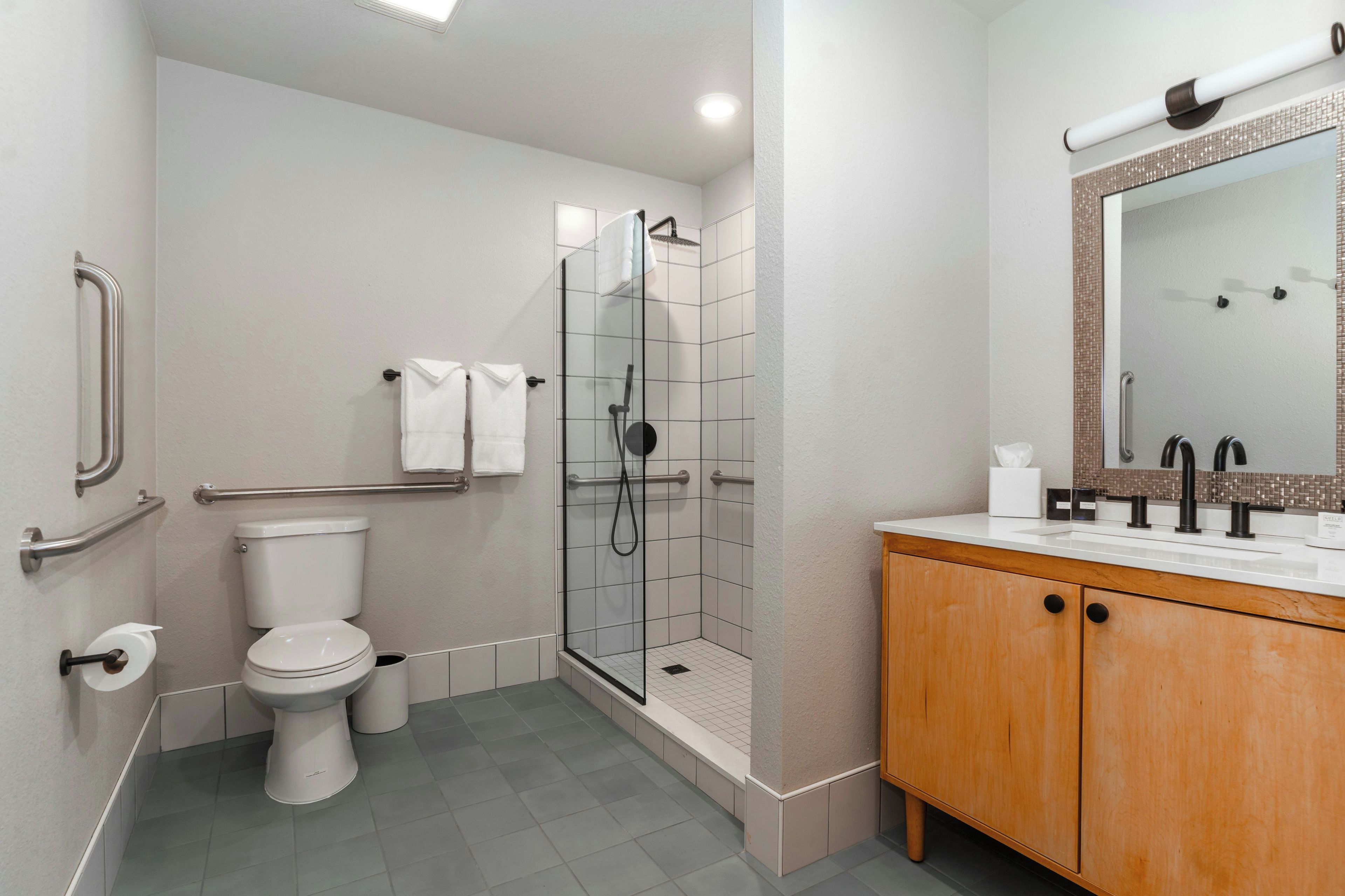 A modern bathroom with a glass-enclosed shower, a white toilet, and a wooden vanity with a mirror.