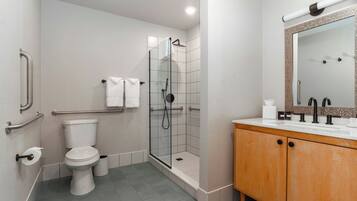A modern bathroom with a glass-enclosed shower, a white toilet, and a wooden vanity with a mirror.