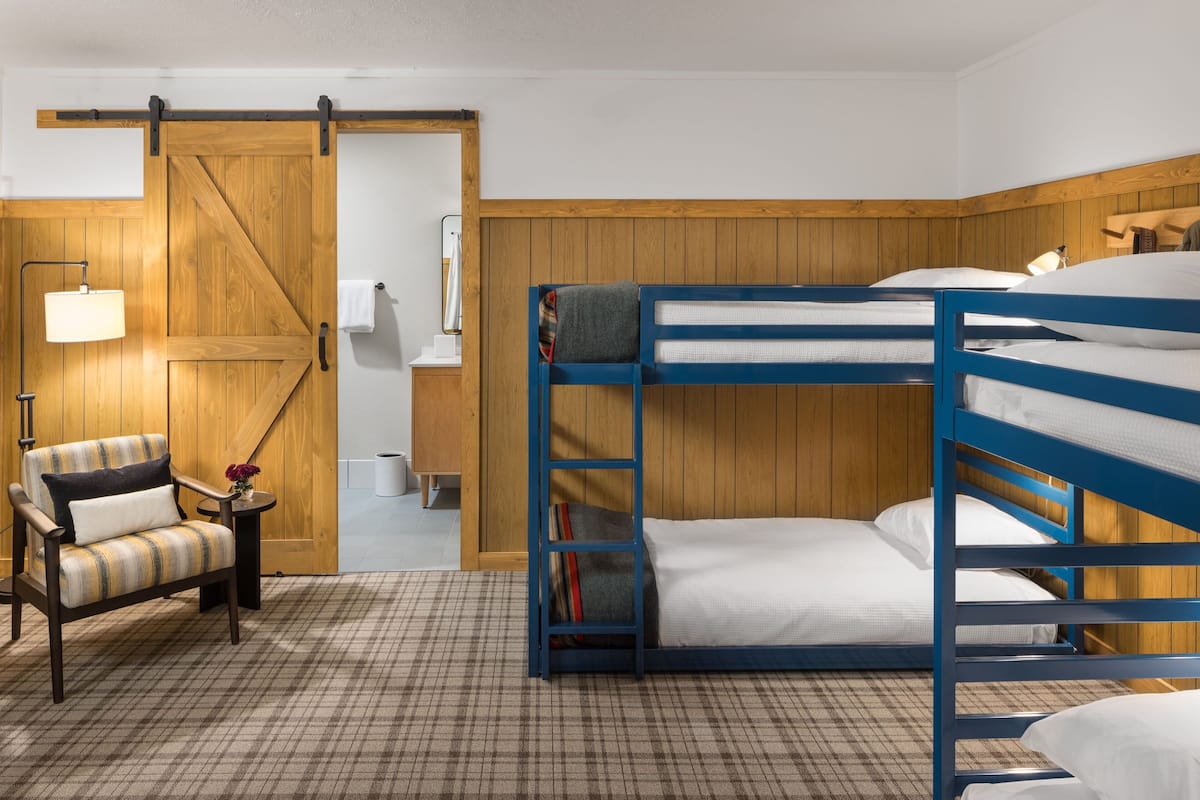 A room with a bunk bed, a chair, a lamp, and a wooden door.