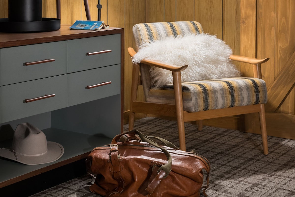 A room with a wooden wall panel, a desk with a lamp, a chair, a television, and a sliding door.