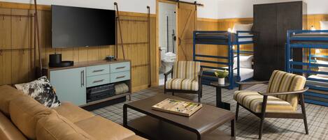 Une chambre meublée comprenant un canapé, des fauteuils, une table basse, un téléviseur, une armoire et un lit superposé.