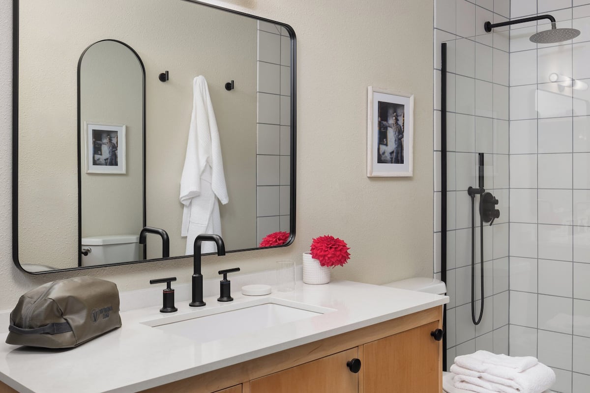 A modern bathroom with a wooden vanity, a large mirror, a white sink, and a shower area.