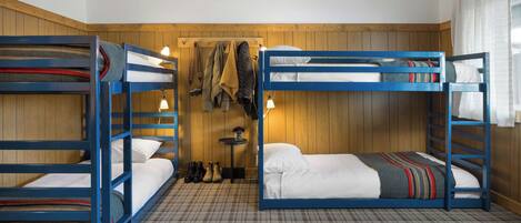 A room with two bunk beds, a small table with a vase, and a coat rack with jackets.