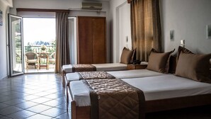 A hotel room with a large bed, a smaller bed, a desk, and a chair. There is a balcony with a table and chairs. - Ilios Hotel (Kassandra)