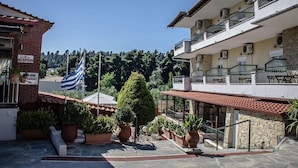 A hotel courtyard with a reception area, outdoor seating, and a flag. - Ilios Hotel (Kassandra)