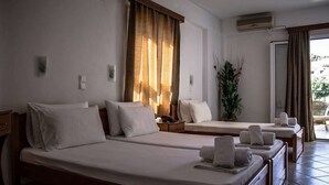 A hotel room with two single beds, a small table, a potted plant, and a view of the outside. - Ilios Hotel (Kassandra)