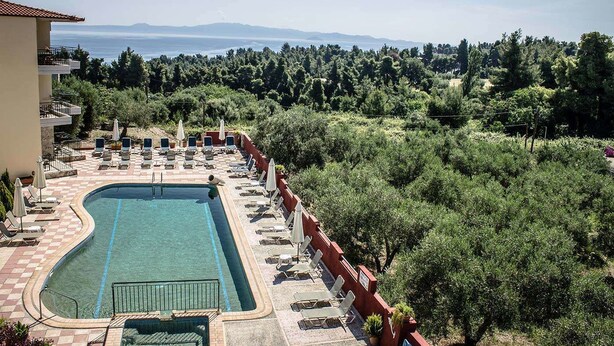 A pool area with lounge chairs and umbrellas, surrounded by trees and a view of the sea and mountains. - Ilios Hotel (Kassandra)