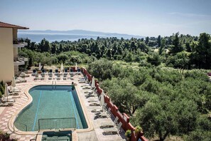 A pool area with lounge chairs and umbrellas, surrounded by trees and a view of the sea and mountains. - Ilios Hotel (Kassandra)